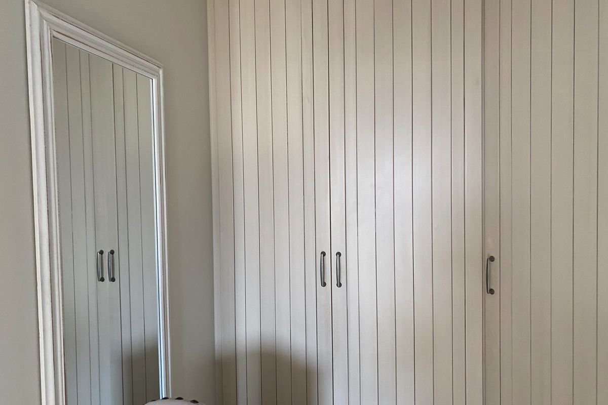 A bedroom featuring floor-to-ceiling built-in wardrobes with vertical panel detailing and a matching full-length mirror.