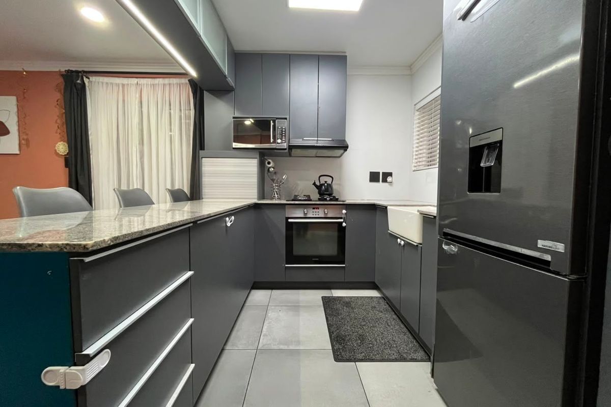 Modern kitchen featuring dark grey cabinetry, granite countertops, an apron sink, and integrated appliances, offering a sleek and functional culinary space.