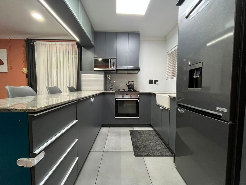 Modern kitchen featuring dark grey cabinetry, granite countertops, an apron sink, and integrated appliances, offering a sleek and functional culinary space.