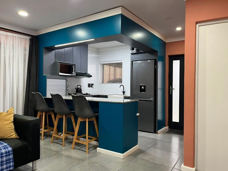 Modern open-plan kitchen featuring bold teal cabinetry, stone countertops, integrated appliances, and sleek tiled flooring, seamlessly connecting to the living area.