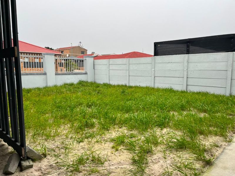 A rear garden area featuring a precast concrete boundary wall and metal security fencing, currently requiring landscaping and lawn maintenance.
