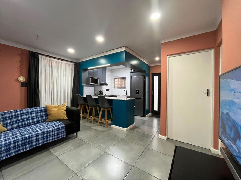 Open-plan living area featuring a modern kitchen with built-in cabinetry, breakfast bar, and tiled flooring throughout.