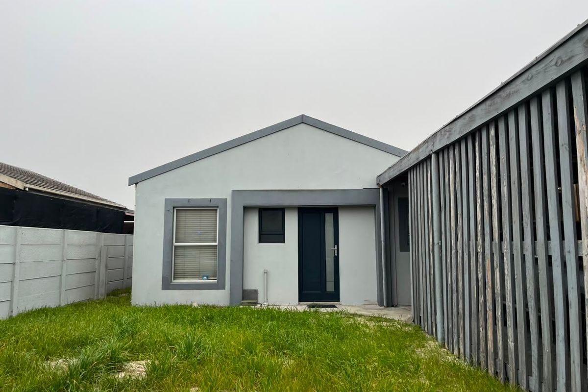 Rear view of the property featuring a small lawn, a timber privacy screen, and a simple exterior facade with a single door and window.