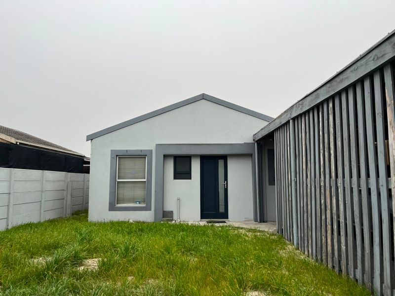 Rear view of the property featuring a small lawn, a timber privacy screen, and a simple exterior facade with a single door and window.