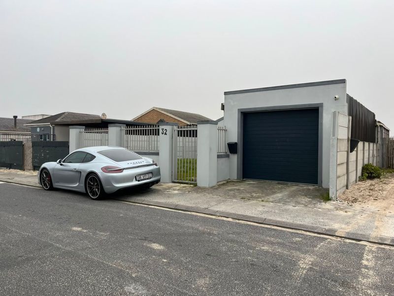 Front exterior view of the property featuring a single garage, perimeter wall with metal gate, and paved driveway access.