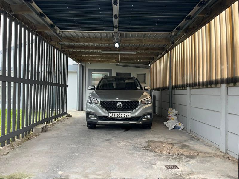 A covered carport or garage area featuring concrete flooring, timber roof structure, and secure perimeter fencing.