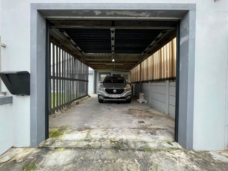 A covered garage area featuring a concrete floor, metal roofing, and perimeter security fencing, showing signs of wear and surface weathering.