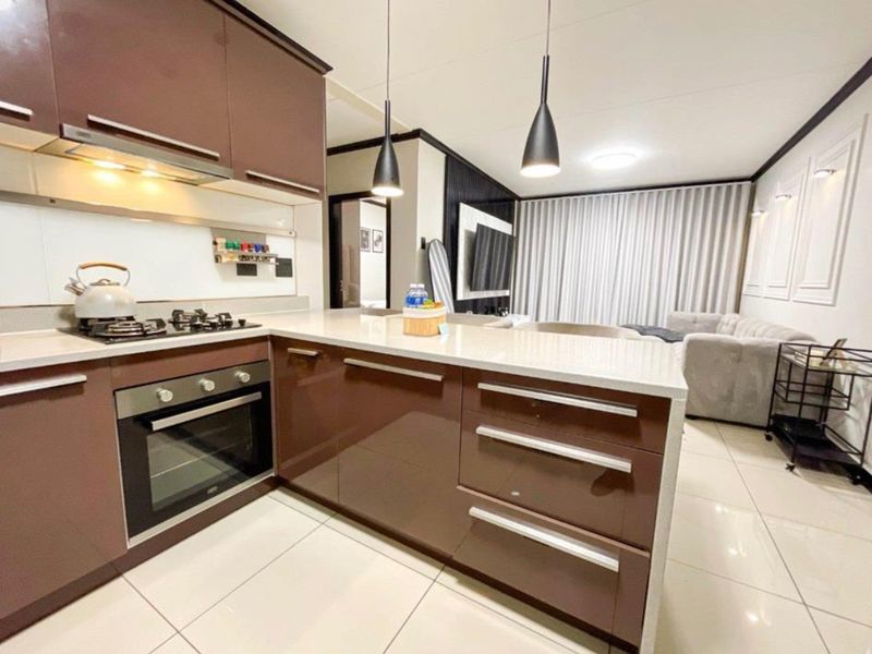 Modern open-plan kitchen and living area featuring high-gloss cabinetry, stone countertops, integrated appliances, and sleek tiled flooring throughout.