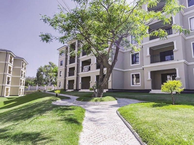 A well-maintained exterior view of a modern apartment complex featuring landscaped lawns, paved walkways, and private balconies.