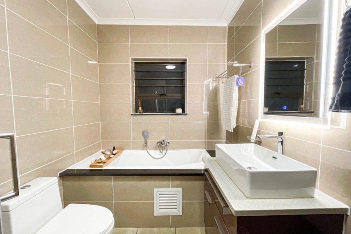 Modern bathroom featuring a built-in bathtub, vessel sink on a vanity cabinet, backlit mirror, and neutral floor-to-ceiling wall tiles.