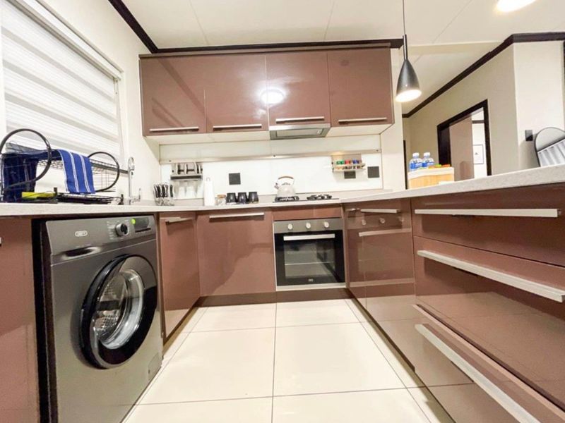 Modern kitchen featuring high-gloss cabinetry, stone countertops, built-in oven, hob, extractor fan, and integrated washing machine with clean tiled flooring.