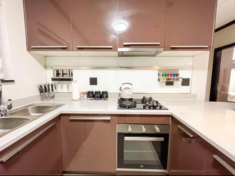 Modern kitchen featuring high-gloss brown cabinetry, stone countertops, a gas hob, built-in oven, and a sleek glass splashback.