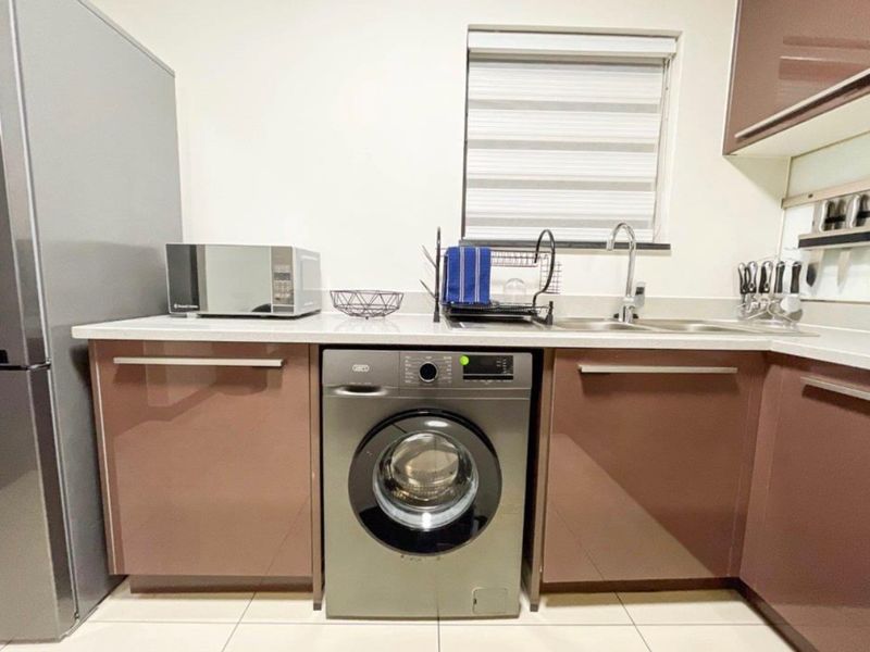 A compact, modern kitchen featuring high-gloss cabinetry, a stainless steel sink with mixer tap, and tiled flooring.