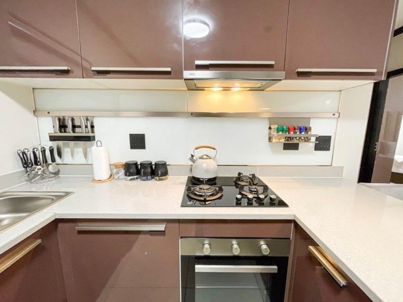 Modern kitchen featuring high-gloss brown cabinetry, stone countertops, integrated gas hob, built-in oven, and a sleek glass splashback.