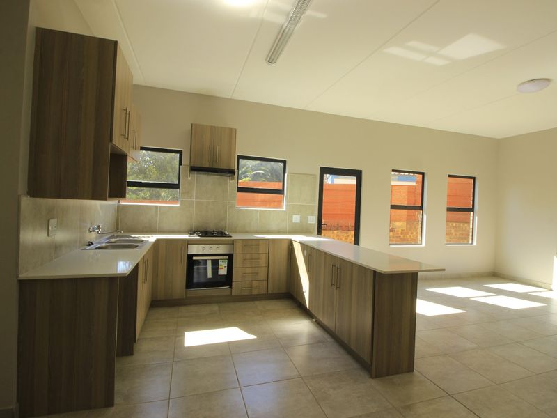 Spacious open-plan kitchen featuring modern wood-finish cabinetry, stone countertops, integrated gas hob, and oven, with ample natural light and tiled flooring throughout.