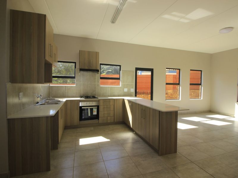Spacious open-plan kitchen and living area featuring modern wood-finish cabinetry, stone countertops, built-in oven, gas hob, and neutral tiled flooring throughout.