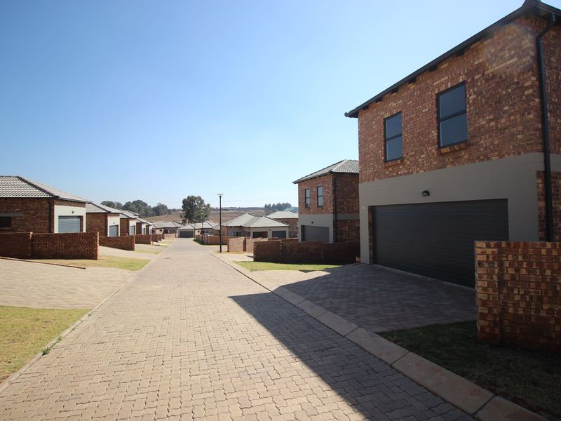 A view of a residential townhouse complex featuring paved driveways, brick facades, and integrated garages under a clear blue sky.
