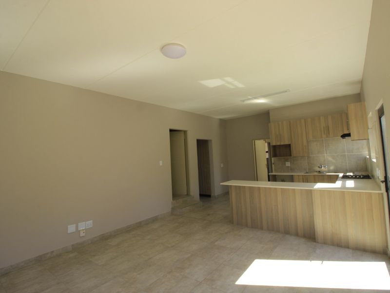 An open-plan living and kitchen area featuring modern wood-finish cabinetry, a breakfast bar, and neutral tiled flooring throughout.