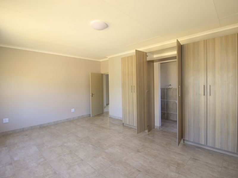 A spacious, empty bedroom featuring neutral tiled flooring, built-in wooden cupboards, and a clean, minimalist aesthetic ready for personalization.