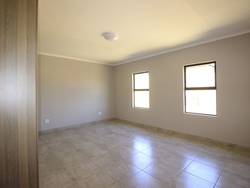 A clean, empty bedroom featuring neutral wall paint, tiled flooring, and a built-in cupboard, offering a blank canvas for personalization.