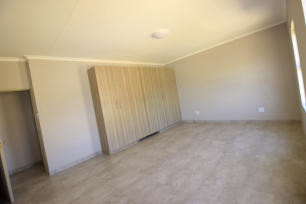 A spacious, empty bedroom featuring neutral tiled flooring and extensive built-in wooden cupboards, offering a clean and versatile living space.