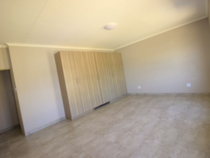 A spacious, empty bedroom featuring neutral tiled flooring and extensive built-in wooden cupboards, offering a clean and versatile living space.