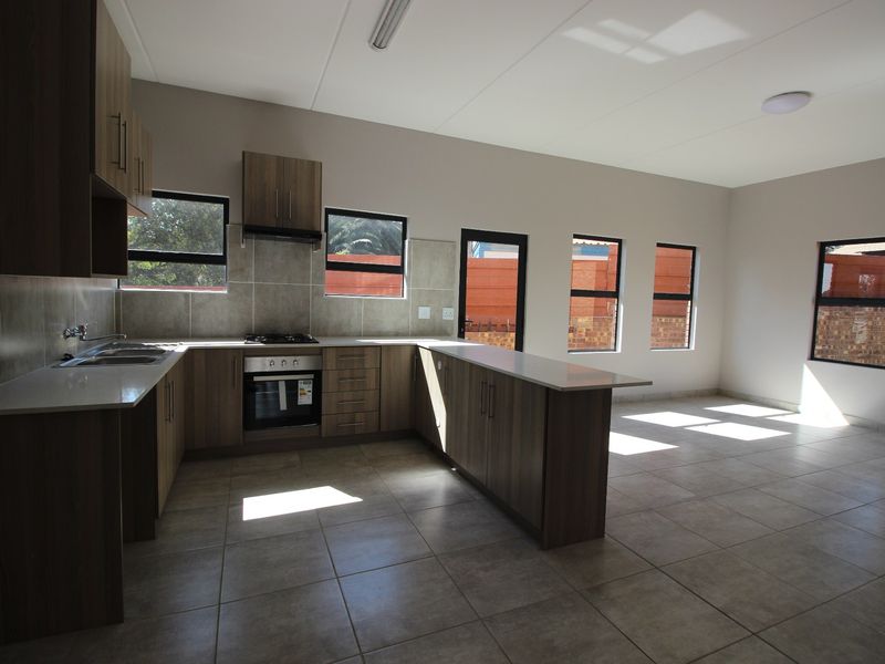 Spacious open-plan kitchen and living area featuring modern cabinetry, stone countertops, built-in appliances, and neutral tiled flooring throughout.