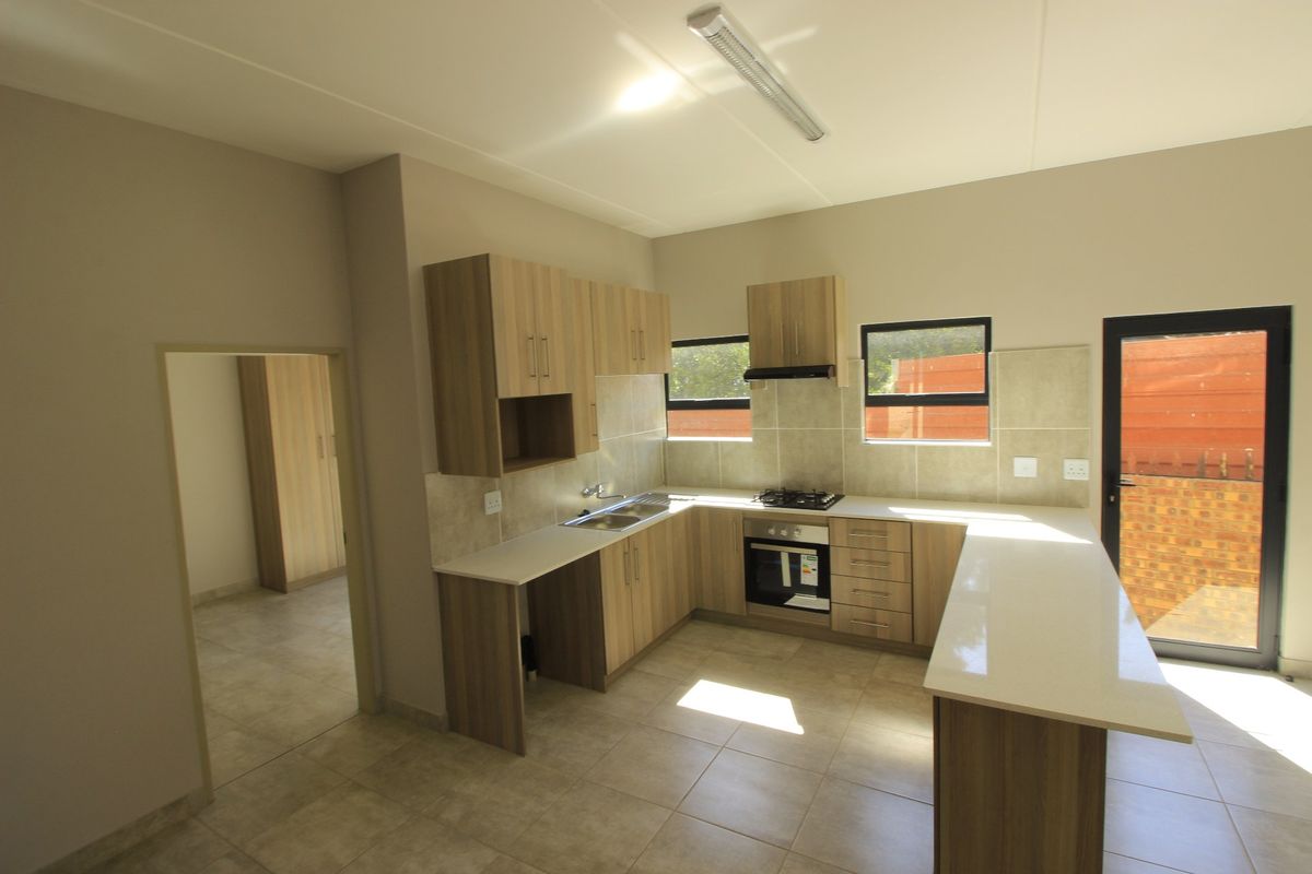 Modern kitchen featuring light wood-finish cabinetry, stone countertops, integrated gas hob, oven, and extractor fan, with tiled flooring and direct access to the exterior.