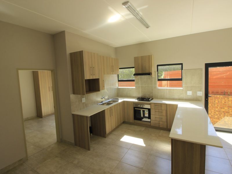 Modern kitchen featuring light wood-finish cabinetry, stone countertops, integrated gas hob, oven, and extractor fan, with tiled flooring and direct access to the exterior.