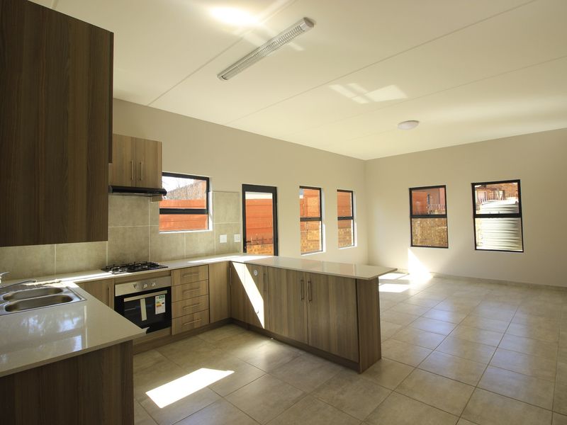 Spacious open-plan kitchen and living area featuring modern wood-finish cabinetry, stone countertops, built-in appliances, and neutral tiled flooring throughout.