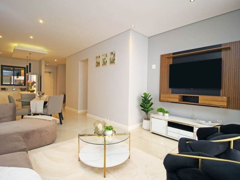 A modern open-plan living and dining area featuring tiled floors, recessed lighting, and a custom built-in media wall unit.