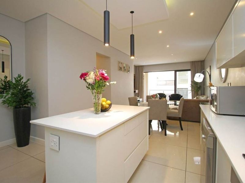 Modern open-plan living area featuring a sleek kitchen island, contemporary pendant lighting, and large format floor tiles leading to a bright living space.