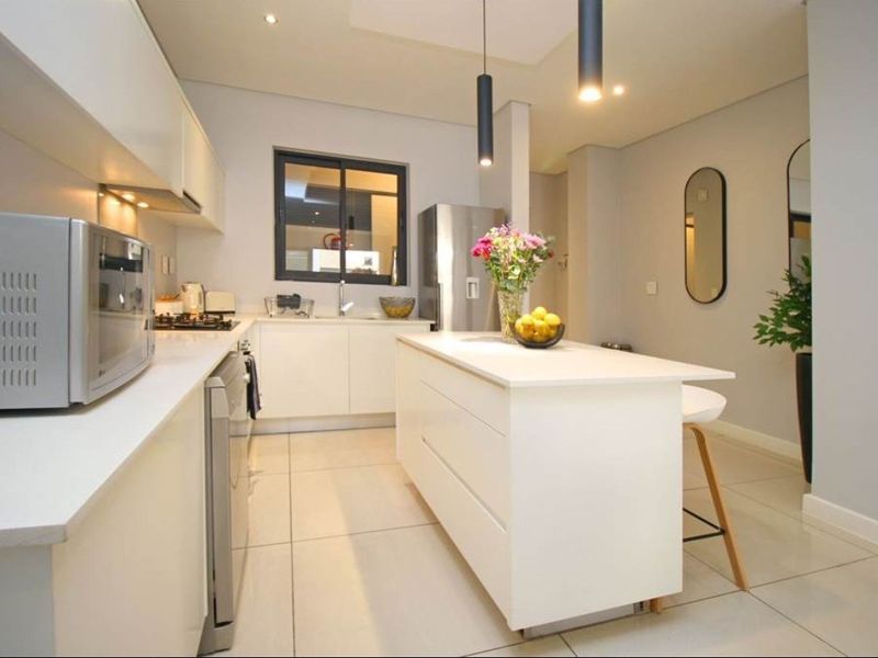Modern kitchen featuring white cabinetry, a central island, gas hob, extractor fan, and tiled flooring with contemporary pendant lighting.