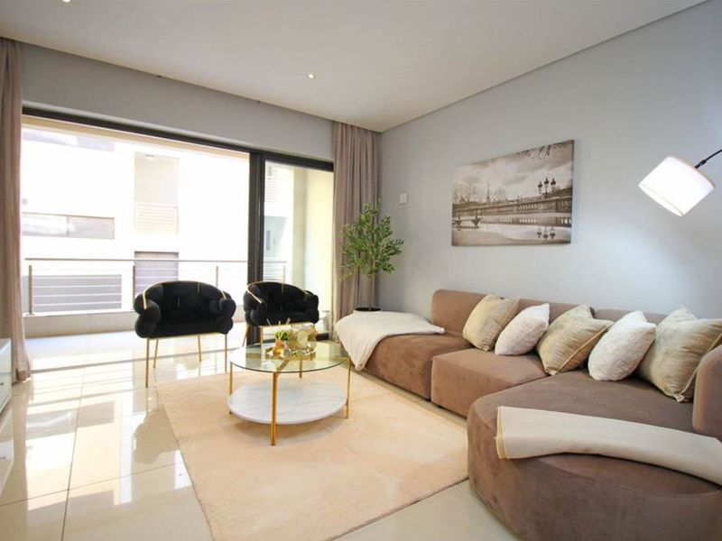A bright and modern living room featuring large sliding glass doors that open onto a private balcony, complemented by polished tiled flooring.