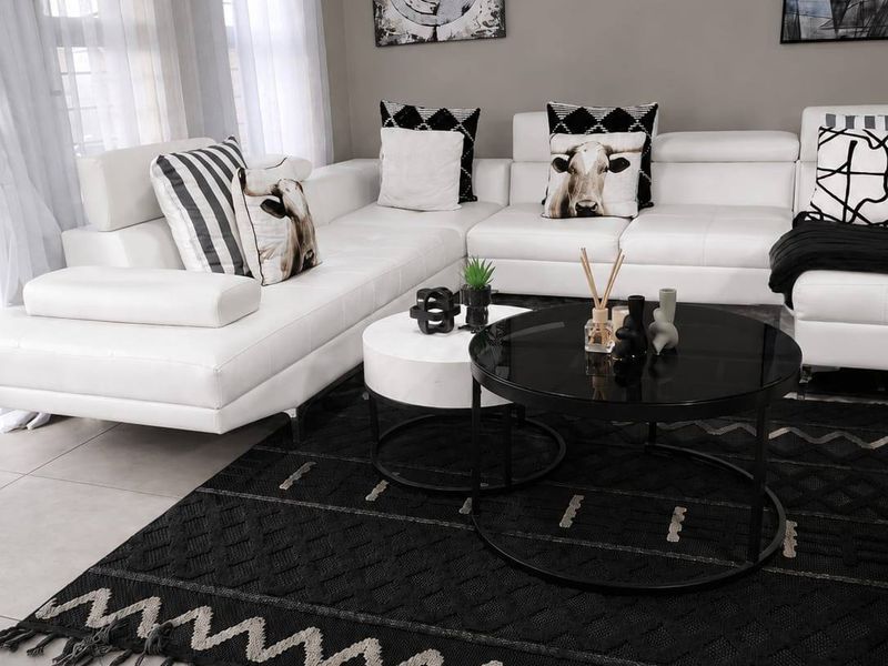 A well-maintained living room featuring neutral tiled flooring, modern cove cornicing, and large windows with installed curtain rods.