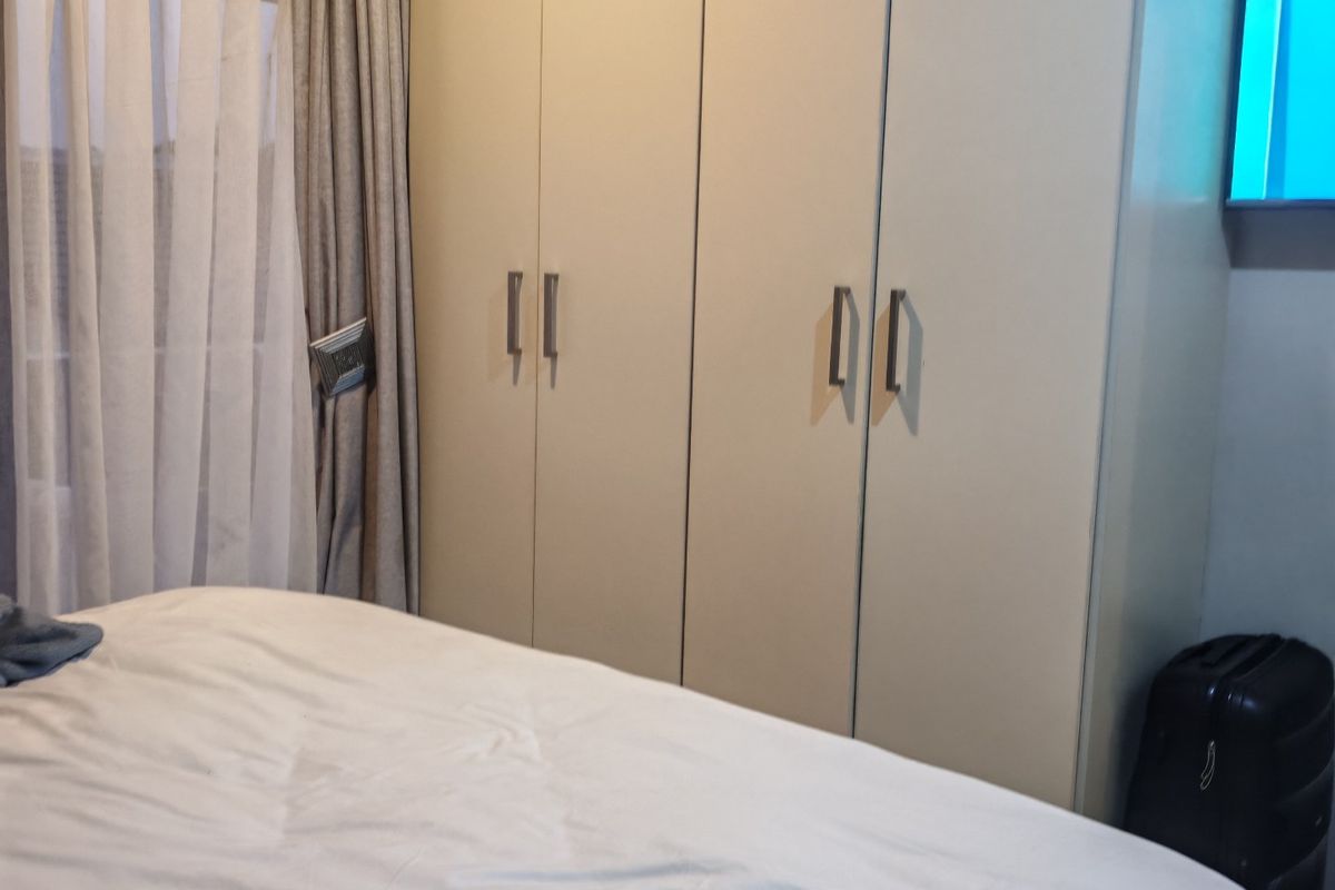 A bedroom featuring neutral-toned built-in cupboards with modern handles and ceiling cornice detailing.