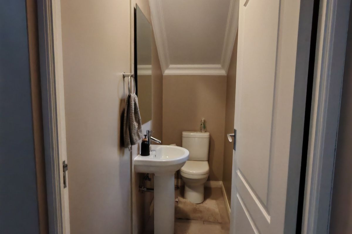 A compact guest bathroom featuring a pedestal sink, toilet, and neutral wall finishes with crown molding detail.