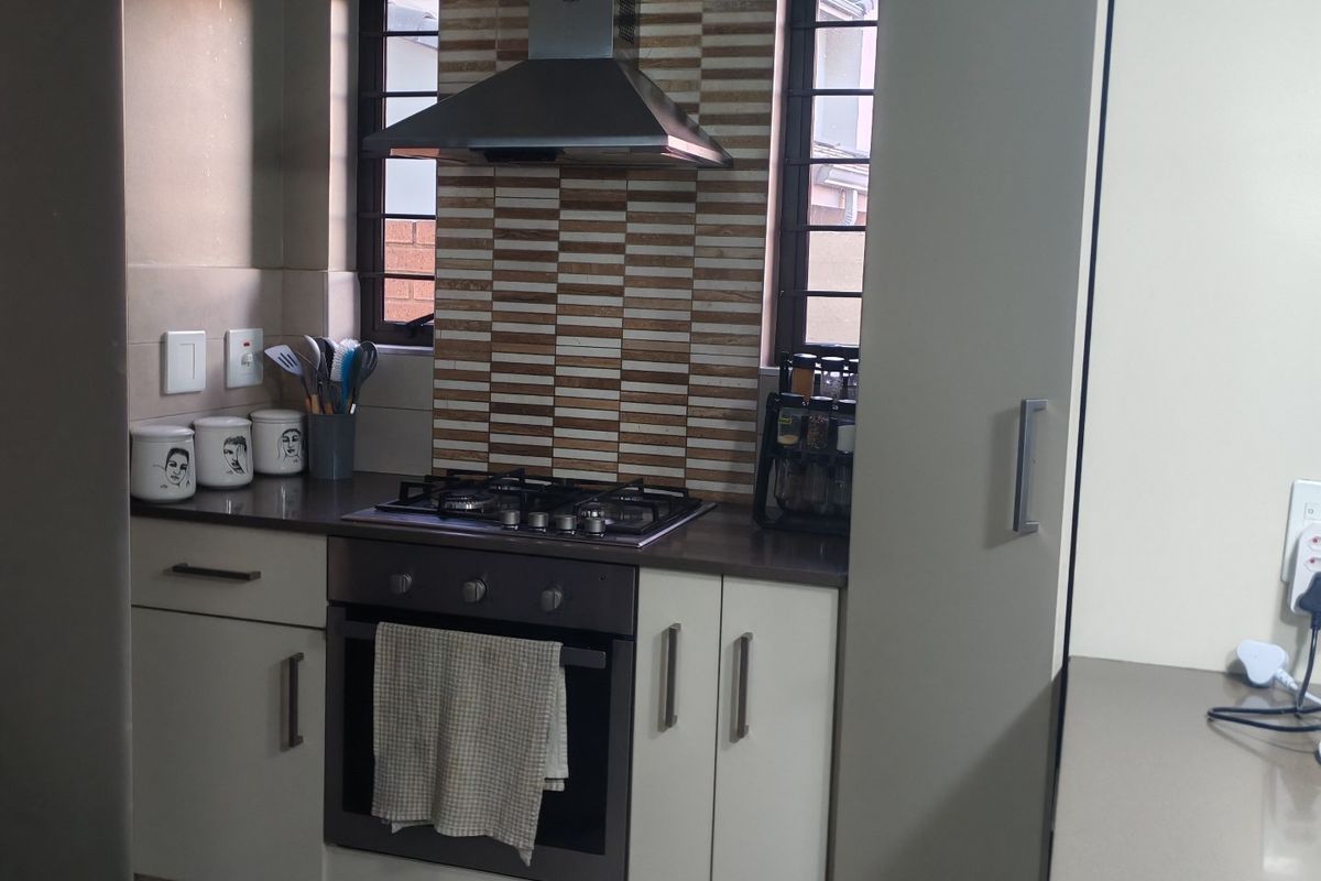 A functional kitchen featuring built-in cabinetry, stone countertops, a gas hob with stainless steel extractor fan, and decorative tiled splashback.