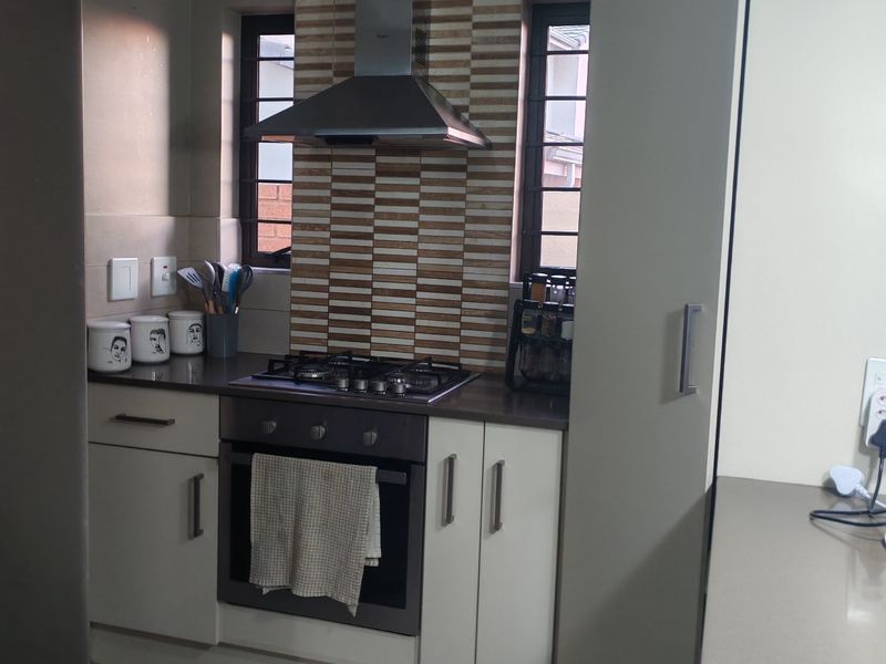 A functional kitchen featuring built-in cabinetry, stone countertops, a gas hob with stainless steel extractor fan, and decorative tiled splashback.