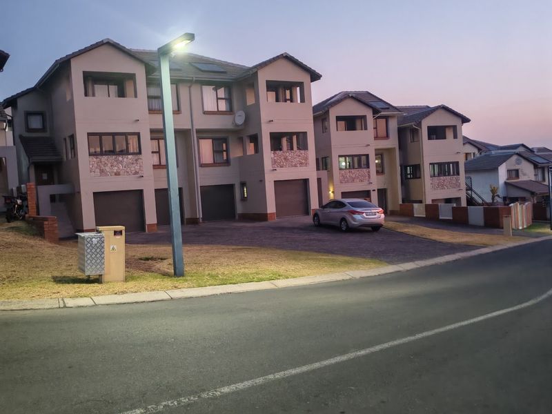 Front elevation of a multi-story townhouse complex featuring paved driveways, integrated garages, stone cladding accents, and balconies at dusk.