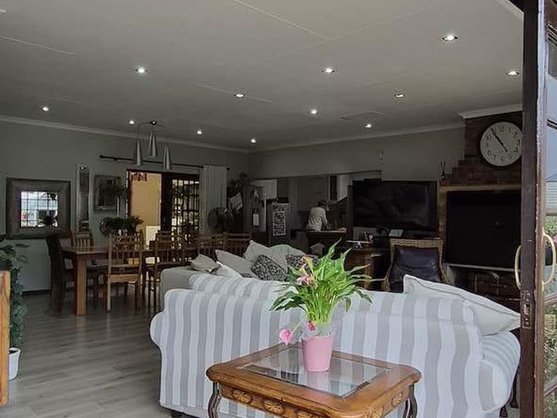 Spacious open-plan living and dining area featuring laminate flooring, recessed lighting, and a brick fireplace, seamlessly connected to the outdoor patio via sliding doors.