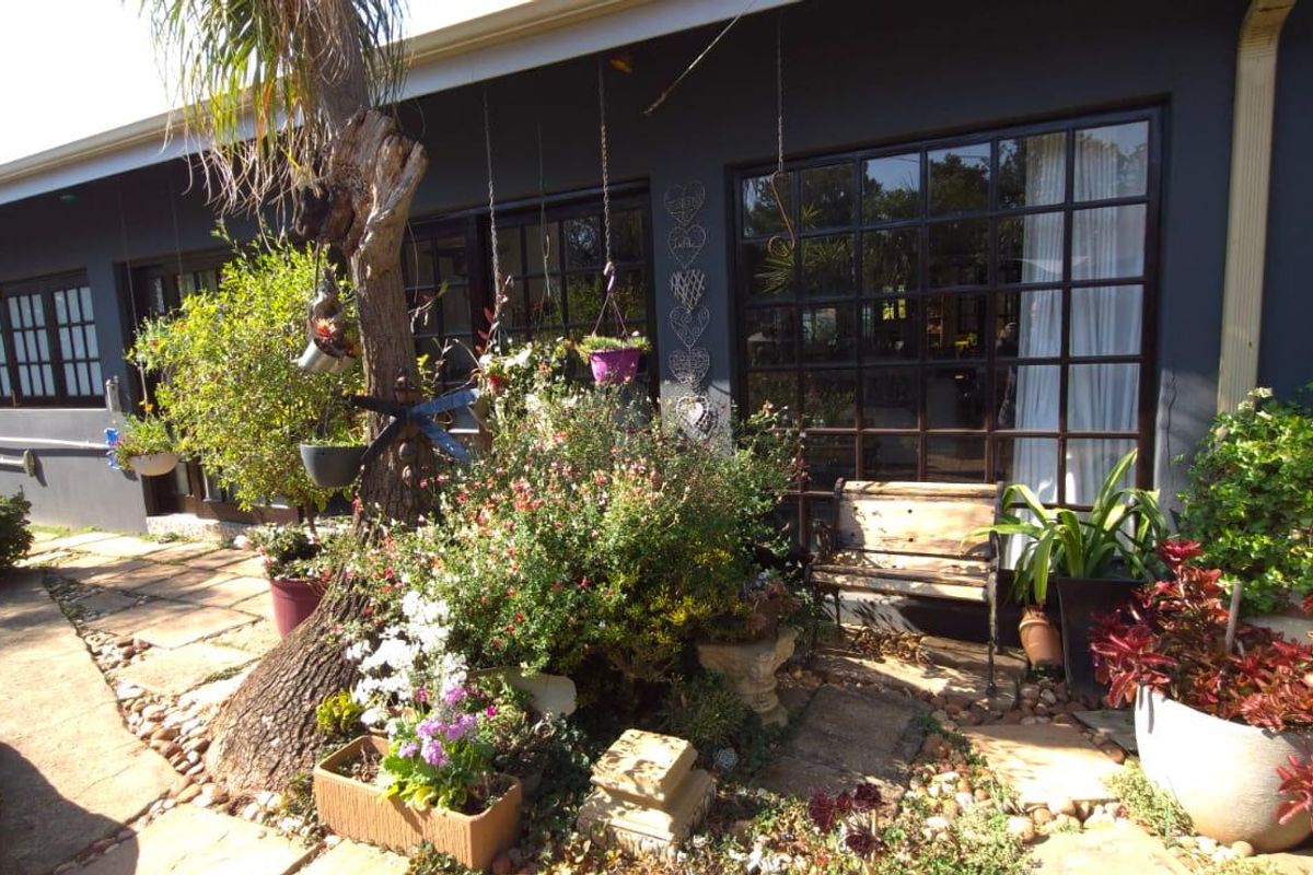 A rear exterior view of the property featuring stone paving, dark-painted walls, and large multi-pane windows overlooking a landscaped garden area.