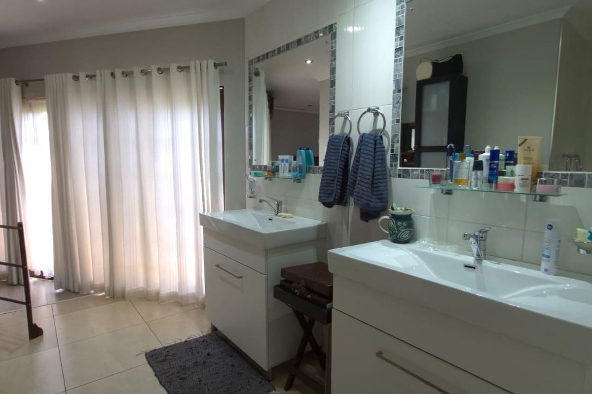 A well-maintained bathroom featuring a double vanity with ceramic basins, tiled walls with mosaic accents, and large mirrors.