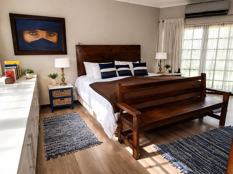 Spacious bedroom featuring laminate flooring, built-in cabinetry, and a wall-mounted air conditioning unit with large windows providing ample natural light.