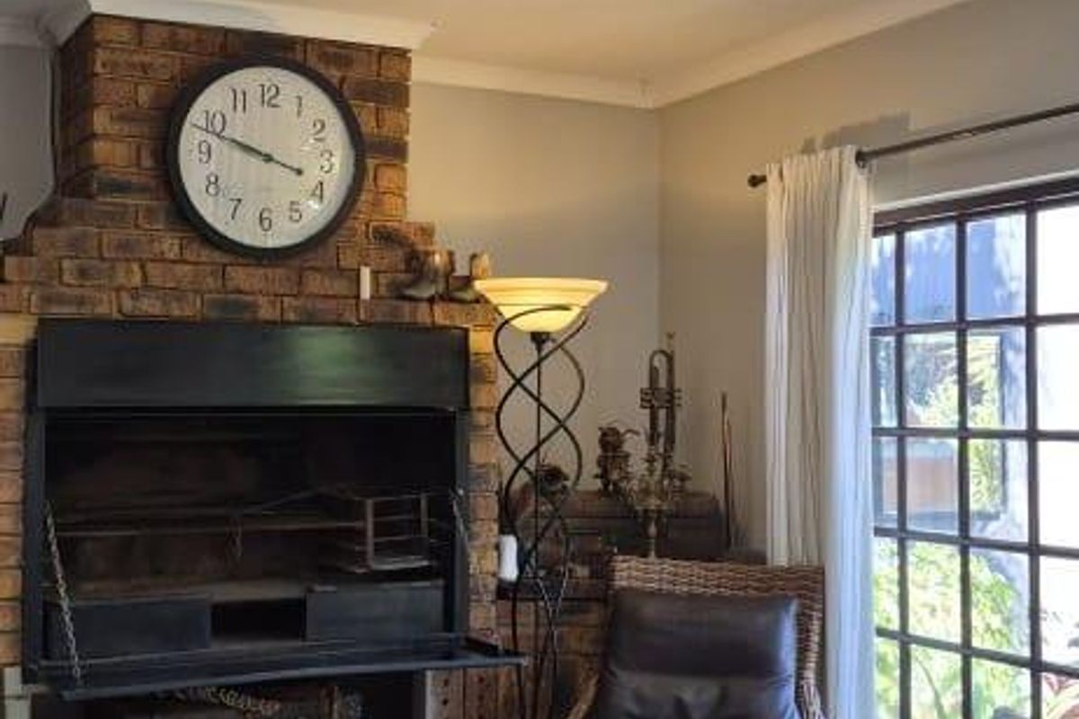 A cozy living room featuring a prominent brick fireplace, modern recessed downlights, and laminate flooring, with direct access to the outdoors through french doors.