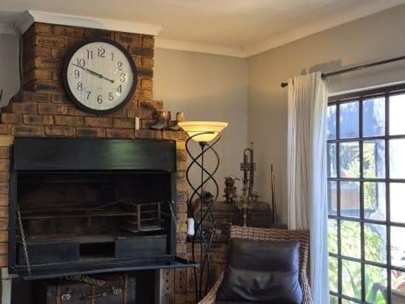 A cozy living room featuring a prominent brick fireplace, modern recessed downlights, and laminate flooring, with direct access to the outdoors through french doors.