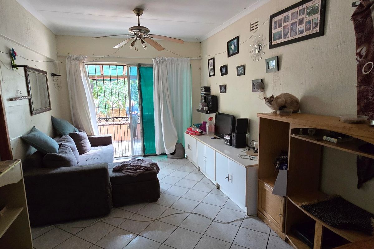 A living room featuring tiled flooring, a ceiling fan, and a sliding glass door leading to an outdoor area with security gate.