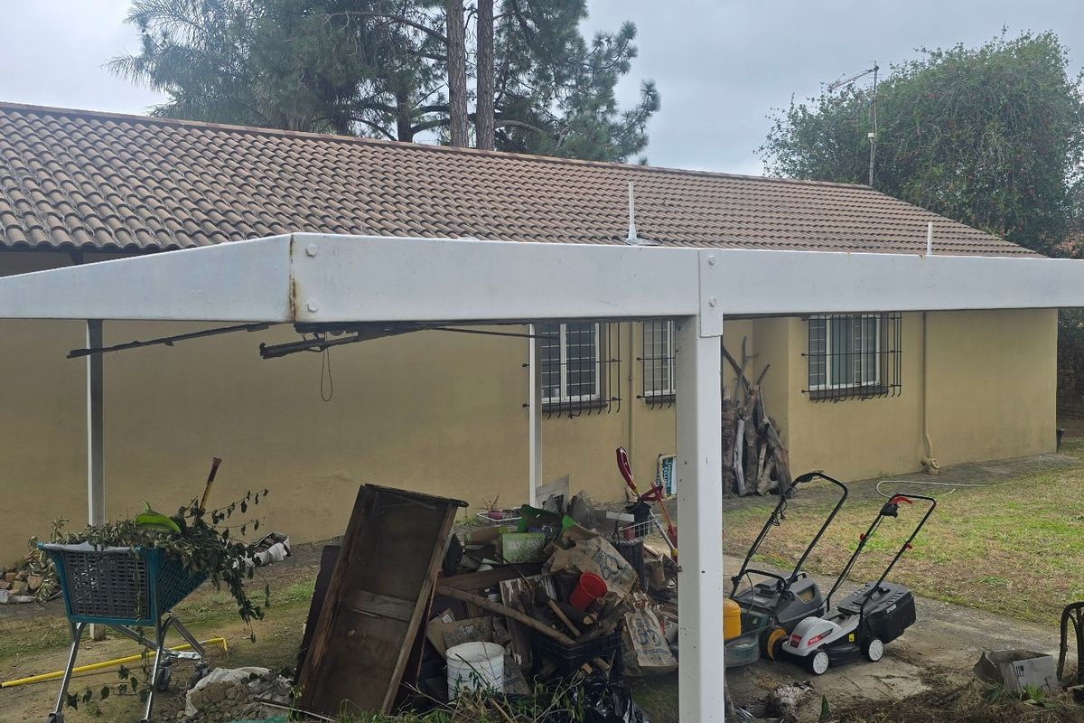 Rear exterior view of the property featuring a metal carport structure with visible signs of rust and security bars on the windows.