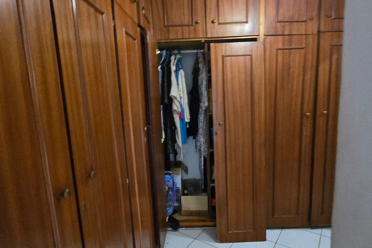 A bedroom featuring extensive floor-to-ceiling built-in wooden cabinetry providing ample storage space, complemented by tiled flooring.