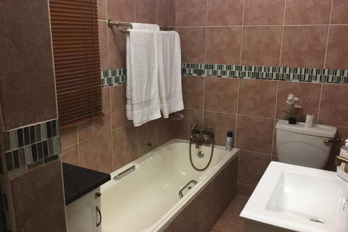 A functional bathroom featuring a bathtub, vanity basin, and toilet with full-height wall tiling and a decorative mosaic border.